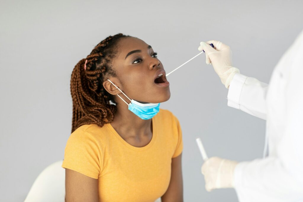 Doctor making oral covid PCR test for young black female patient over grey studio background